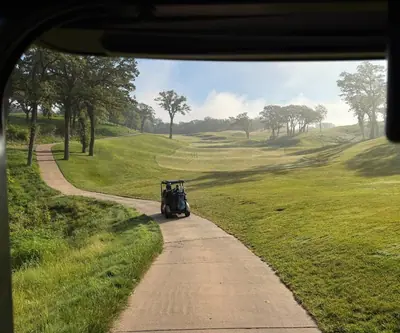 View from a golf cart of a curving cart path and misty rolling fairway at Quarry Oaks Golf Club in Ashland, Nebraska
