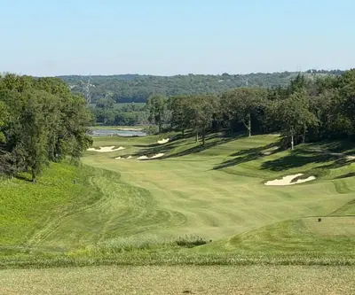 Elevated view down a bunkered fairway toward distant water and wooded bluffs at Quarry Oaks Golf Club in Ashland, Nebraska