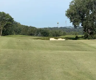 Fairway rolling toward a bunker and yellow flag, water tower beyond, at Quarry Oaks Golf Club in Ashland, Nebraska