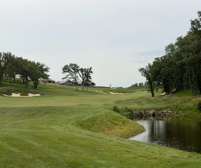 Fairway beside a stone-edged pond with bunkers and the clubhouse beyond at Quarry Oaks Golf Club in Ashland, Nebraska