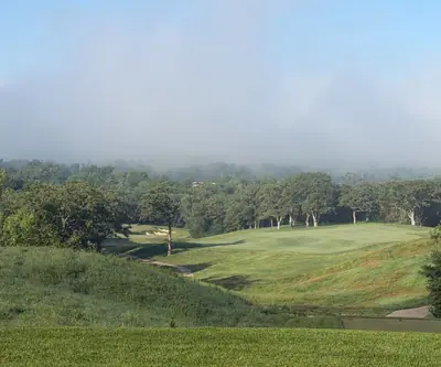 Morning fog hangs over rolling fairways, oak trees and a distant bunker at Quarry Oaks Golf Club in Ashland, Nebraska