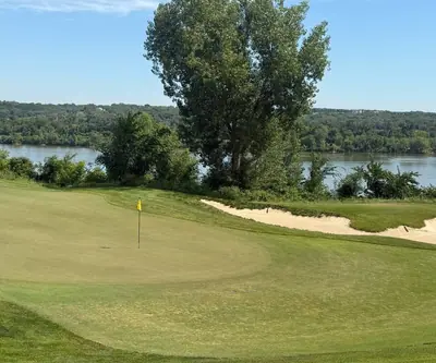 Green with yellow flag and bunker above a river and wooded bluffs at Quarry Oaks Golf Club in Ashland, Nebraska