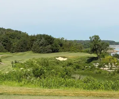 Bunkered green beyond native wildflowers with a river in the distance at Quarry Oaks Golf Club in Ashland, Nebraska