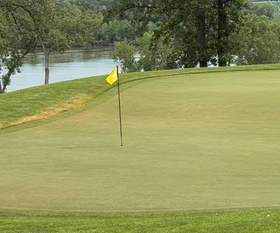 Yellow flag on a green beside a river and tall trees at Quarry Oaks Golf Club in Ashland, Nebraska