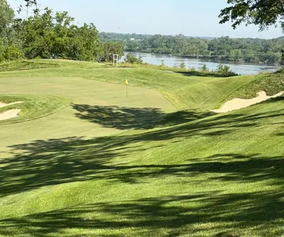 Bunker-guarded green with a yellow flag overlooking a wide river at Quarry Oaks Golf Club in Ashland, Nebraska