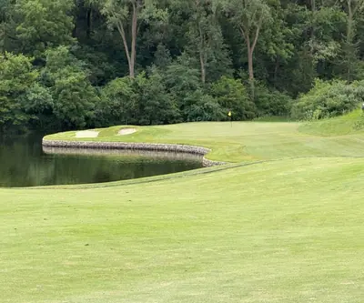 Green with a yellow flag behind a stone-walled pond and two bunkers at Quarry Oaks Golf Club in Ashland, Nebraska