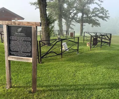 Historic cemetery sign and iron-fenced pioneer grave markers on a foggy morning at Quarry Oaks Golf Club in Ashland, Nebraska