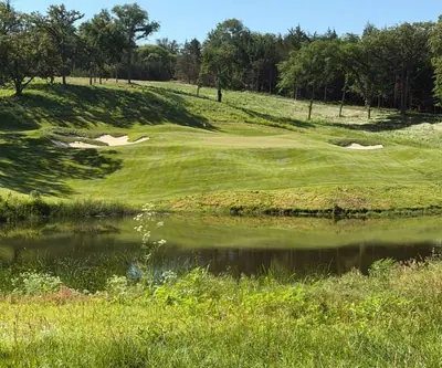 Pond in front of a rolling approach with bunkers below a wooded ridge at Quarry Oaks Golf Club in Ashland, Nebraska