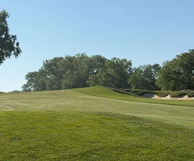 Sloping fairway rising past a grass-faced bunker toward mature trees at Quarry Oaks Golf Club in Ashland, Nebraska