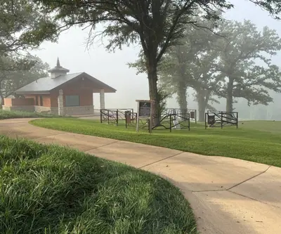 Stone-and-brick shelter and sign beside a curving cart path in fog at Quarry Oaks Golf Club in Ashland, Nebraska