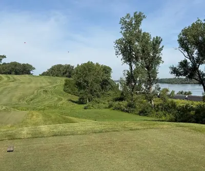Tee view of a rolling hillside fairway beside a wide river framed by trees at Quarry Oaks Golf Club in Ashland, Nebraska