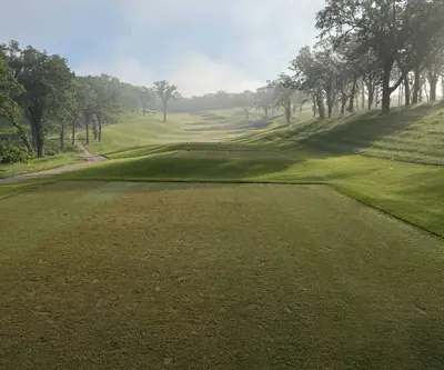 Tee box looking down a fog-filled valley fairway framed by mature trees at Quarry Oaks Golf Club in Ashland, Nebraska