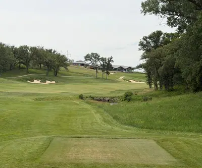 Tee box view down a tree-lined hole toward the hilltop clubhouse at Quarry Oaks Golf Club in Ashland, Nebraska