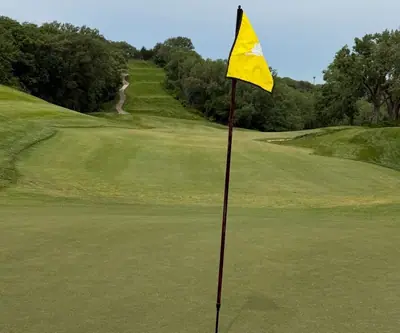 Yellow flag on a green looking back up a steep tree-lined fairway at Quarry Oaks Golf Club in Ashland, Nebraska