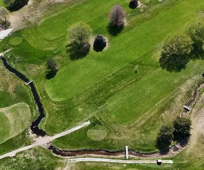 Aerial view of a creek winding past greens and fairways with footbridges at Poco Creek Golf Course in Aurora, Nebraska