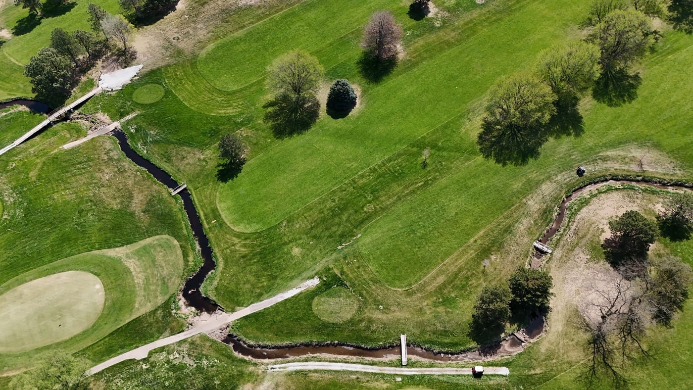 Aerial view of a creek winding past greens and fairways with footbridges at Poco Creek Golf Course in Aurora, Nebraska
