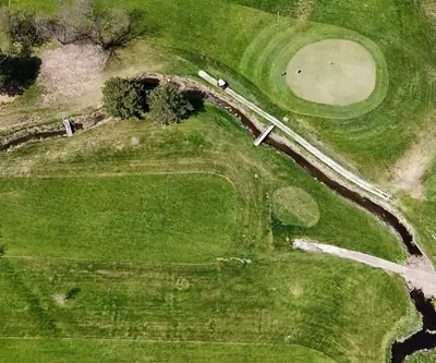 Aerial view of a creek winding past a green, footbridges, and cart path at Poco Creek Golf Course in Aurora, Nebraska