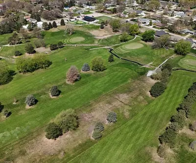 Aerial view of tree-lined fairways and greens bordered by a neighborhood at Poco Creek Golf Course in Aurora, Nebraska