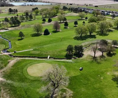 Aerial view of a green, winding creek, cart paths and tree-lined fairways at Poco Creek Golf Course in Aurora, Nebraska