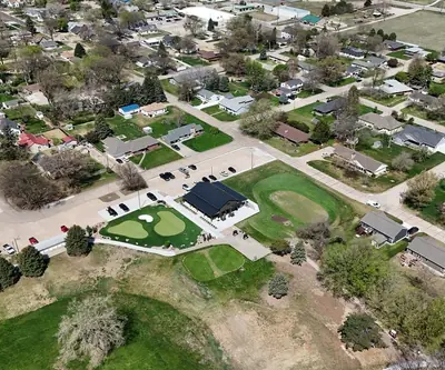 Aerial view of putting greens and a dark-roofed building among homes at Poco Creek Golf Course in Aurora, Nebraska