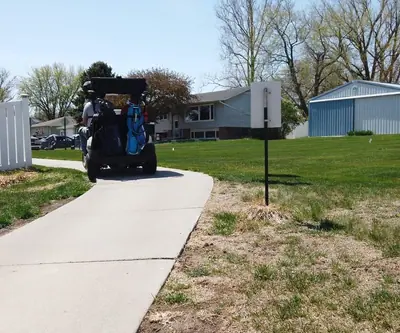 Golf cart on a concrete cart path past a white fence and homes at Poco Creek Golf Course in Aurora, Nebraska