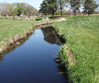 Narrow creek winding between grassy banks toward a footbridge at Poco Creek Golf Course in Aurora, Nebraska