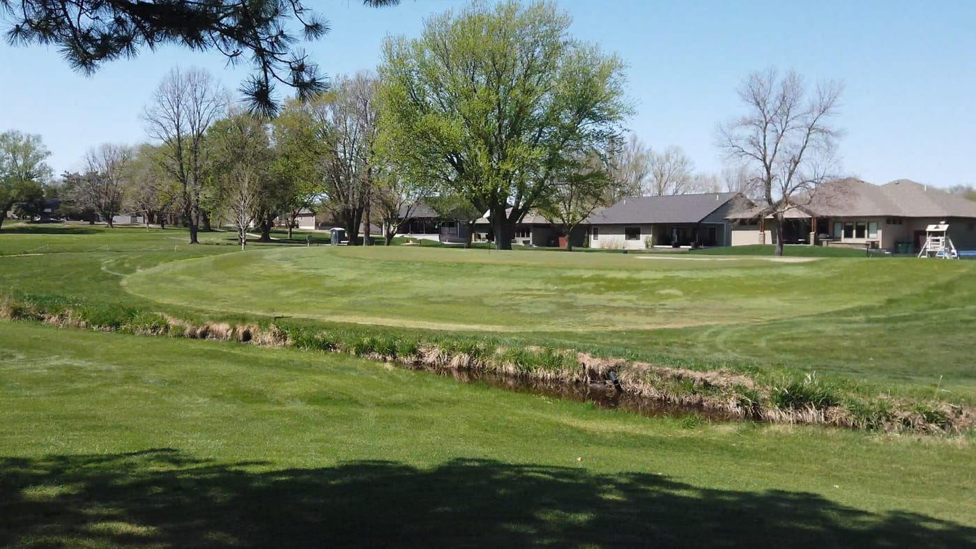 Creek running in front of a green lined by homes and trees at Poco Creek Golf Course in Aurora, Nebraska