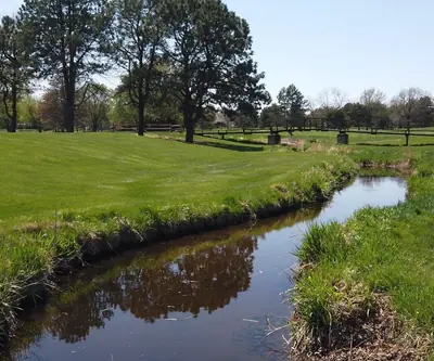 Creek winding through fairways toward a wooden footbridge at Poco Creek Golf Course in Aurora, Nebraska