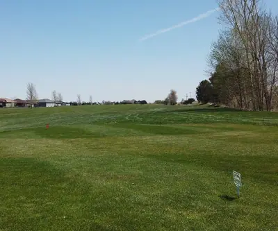 Tee area with a red marker and small sign facing a wide fairway lined by homes at Poco Creek Golf Course in Aurora, Nebraska
