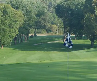 Checkered blue and white flag on a green with a tree-lined fairway behind at Indian Trails Country Club in Beemer, Nebraska