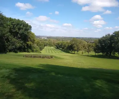 Downhill view of a striped fairway framed by trees and a distant valley at Indian Trails Country Club in Beemer, Nebraska