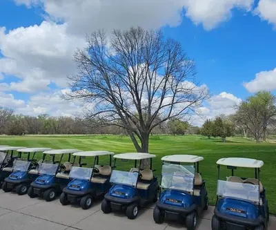 Row of blue golf carts lined up beside a fairway under puffy clouds at Cross Creek Golf Links in Cambridge, Nebraska