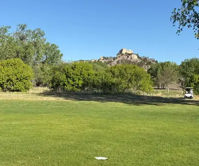 Sandstone butte rising above trees behind a fairway with a golf cart at Legend Buttes Golf Course in Crawford, Nebraska