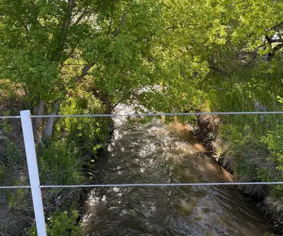 Creek flowing beneath shade trees, seen from a white-railed bridge at Legend Buttes Golf Course in Crawford, Nebraska
