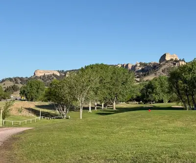 Tree-lined fairway with a red tee marker below sandstone buttes at Legend Buttes Golf Course in Crawford, Nebraska