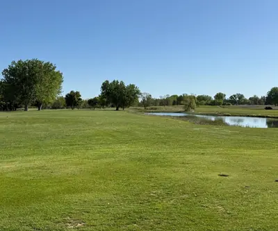Open fairway alongside a calm pond under a clear blue sky at Legend Buttes Golf Course in Crawford, Nebraska