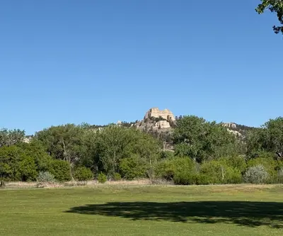 Sandstone butte rising above a line of trees beyond open turf at Legend Buttes Golf Course in Crawford, Nebraska
