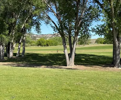 Tall shade trees framing a fairway with rocky buttes in the distance at Legend Buttes Golf Course in Crawford, Nebraska