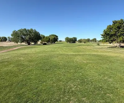 Wide fairway with a dirt cart path and scattered trees under clear sky at Legend Buttes Golf Course in Crawford, Nebraska