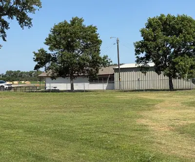White building and metal shed behind shade trees and picnic tables at Dannebrog Country Club in Dannebrog, Nebraska
