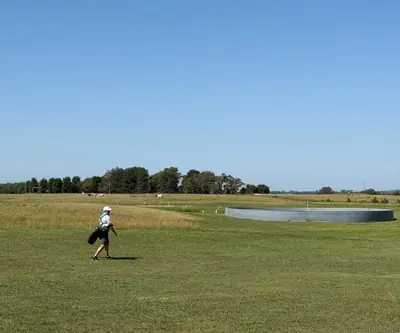 Golfer carrying a bag toward a flag beside a round steel ring at Dannebrog Country Club in Dannebrog, Nebraska