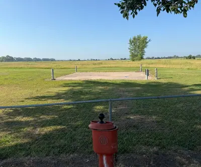 Red ball washer by a chain-link fence facing a dirt pad and open prairie at Dannebrog Country Club in Dannebrog, Nebraska