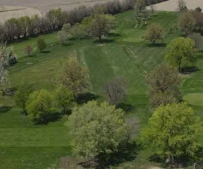 Aerial view of tree-lined fairways and greens beside farm fields at Falls City Golf Course in Falls City, Nebraska