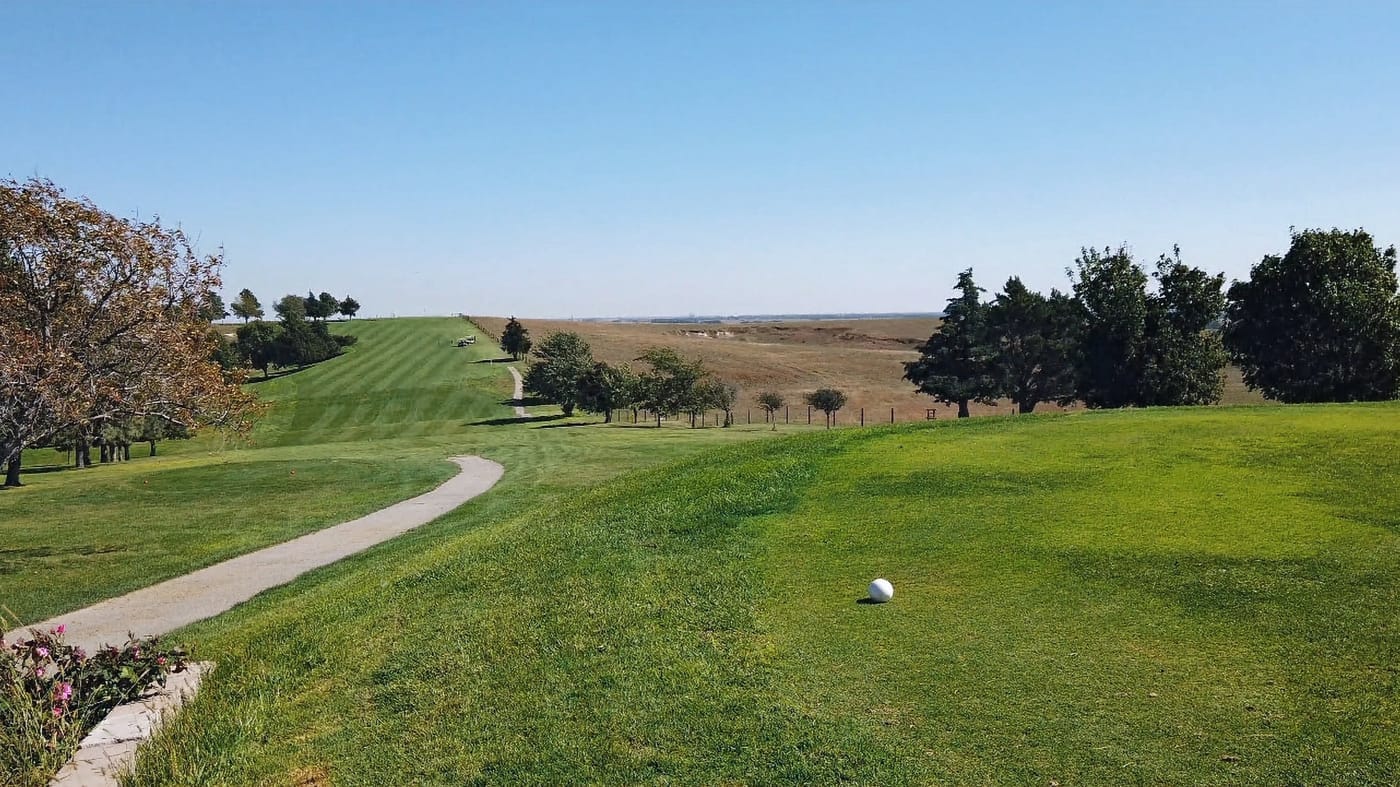 Golf course scene with a ball on green grass, winding path, trees, and expansive blue sky. Peaceful and serene setting.  Hole #1 at Gibbon Valley View Golf Course