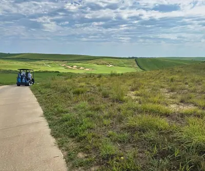 Golf cart on a concrete path above native grass and a bunkered hole at Landmand Golf Club in Homer, Nebraska