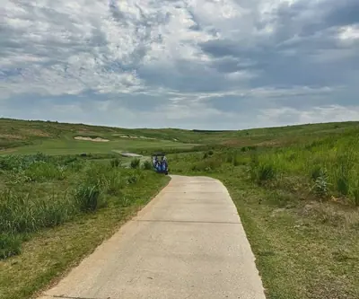 Cart path leading past a parked cart toward rolling fairways and bunkers at Landmand Golf Club in Homer, Nebraska