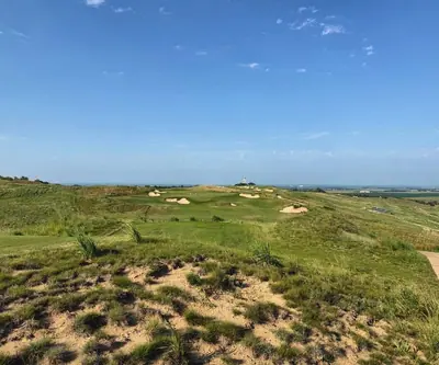 Elevated view over sandy dunes toward a heavily bunkered green at Landmand Golf Club in Homer, Nebraska