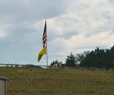 American and yellow flags flying above a grassy hillside and rail fence at Landmand Golf Club in Homer, Nebraska