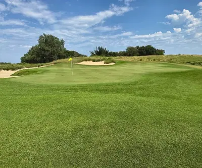 Rolling green with a yellow flag, sand bunkers and native grass at Landmand Golf Club in Homer, Nebraska