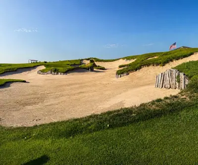 Massive sand bunker with wooden plank walls and an American flag above at Landmand Golf Club in Homer, Nebraska